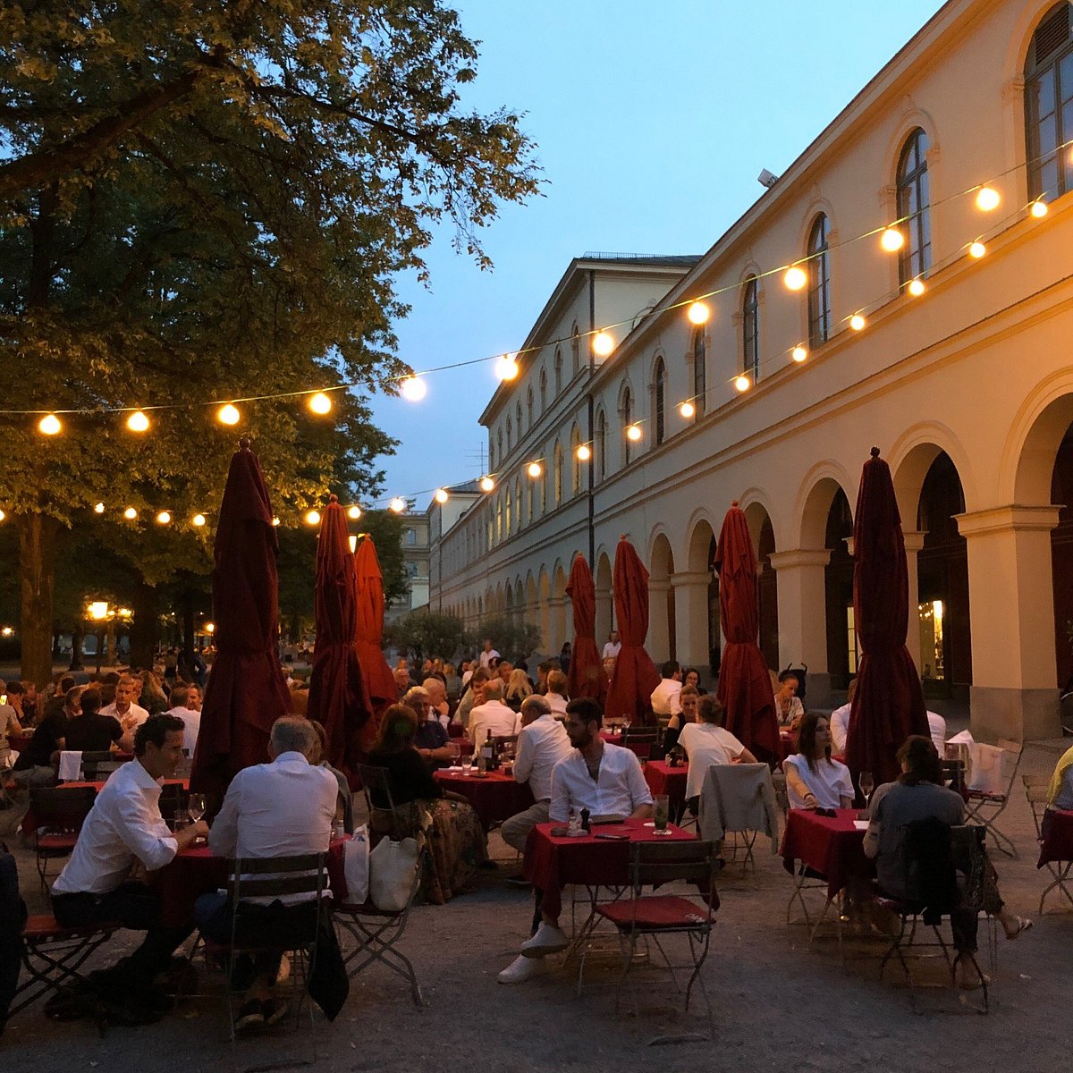 Lively Munich outdoor dining in the evening beneath illuminated historic arcades